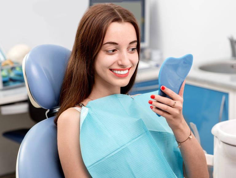 Young woman patient after cosmetic dental treatment looking at her teeth in the mirror.