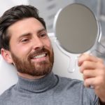 Man in a dental chair looking at his new dental implants in a mirror