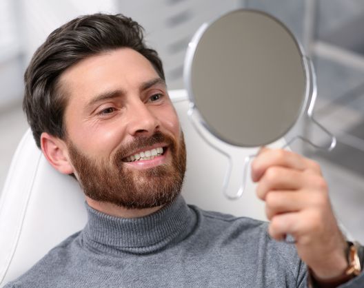 Man in a dental chair looking at his new dental implants in a mirror