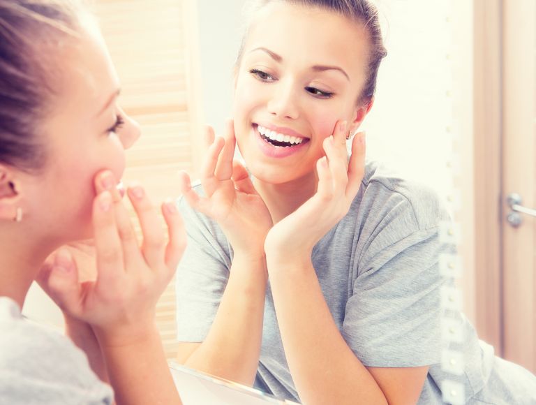 Young woman with beautiful healthy teeth looking at her smile in a bathrooma mirror.