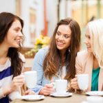 three young women with perfect smiles chatting and having coffee at a cafe