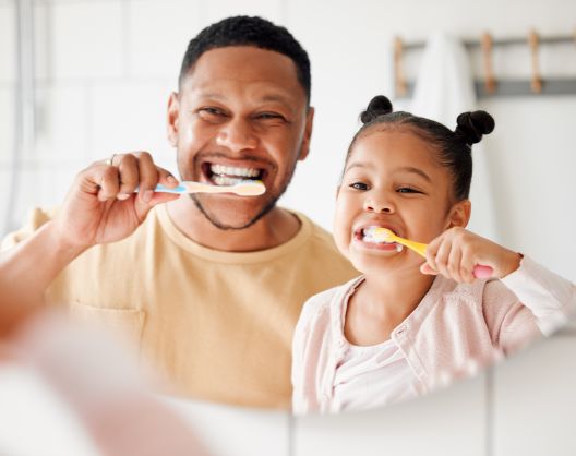 An aFro American dad and little girl having fun while brushing teeth together in front of the bathroom mirror