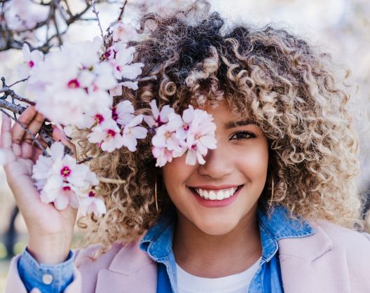 Happy young woman with a perfect smile posing to a photo touching a branch of blooming tree