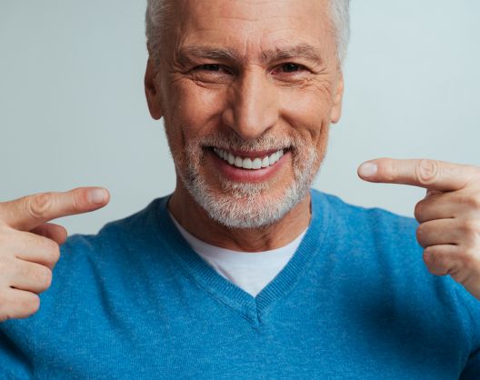 Happy senior man with a perfect smile pointing at his teeth